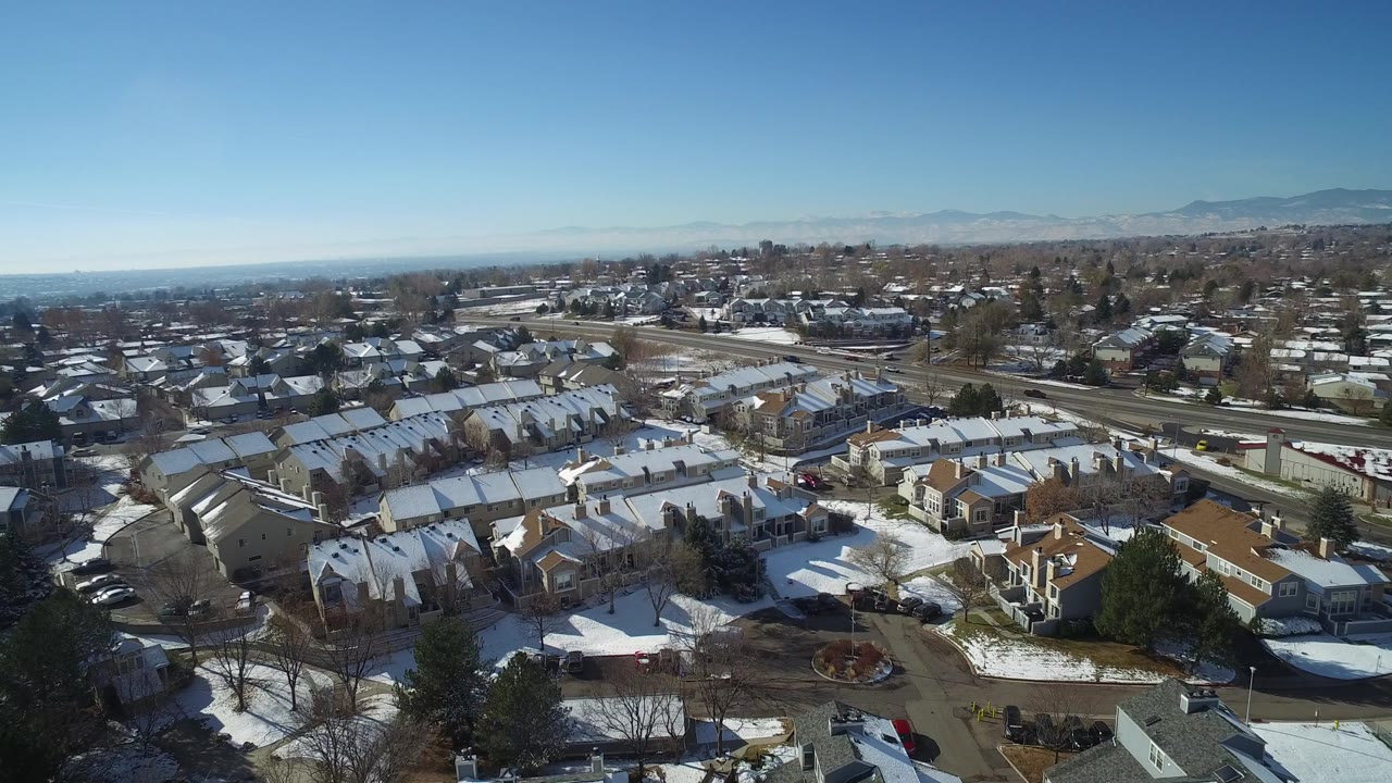 Wide aerial of suburban rooftops with mountains on the horizon.