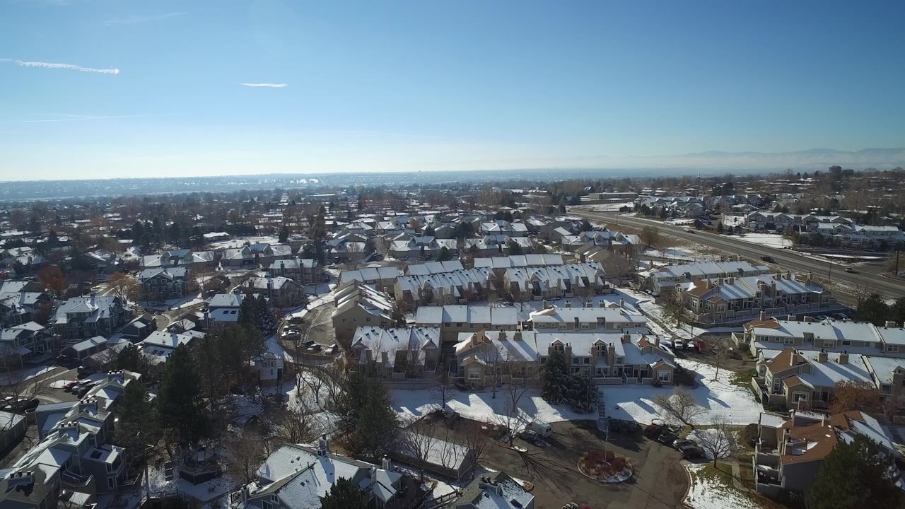 Aerial view over snow-covered suburban homes under a blue sky.