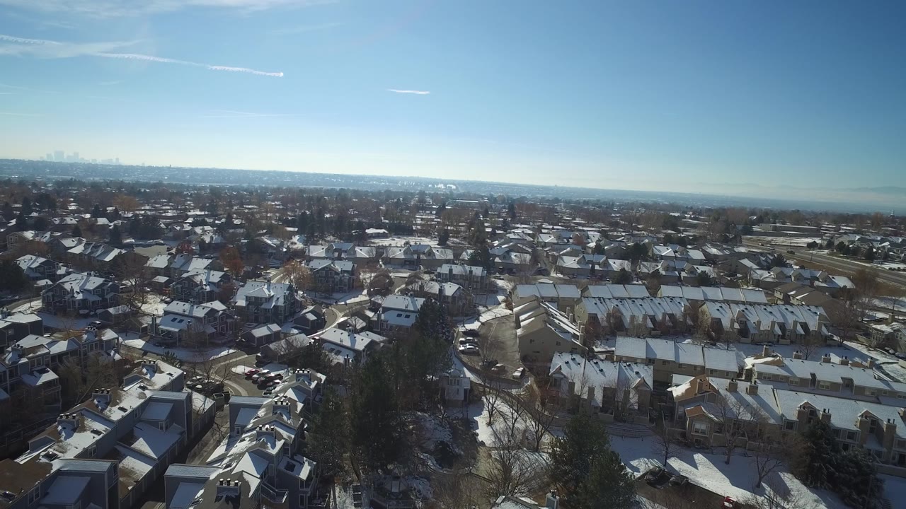 Drone view over a residential area with snowy roofs and distant skyline.