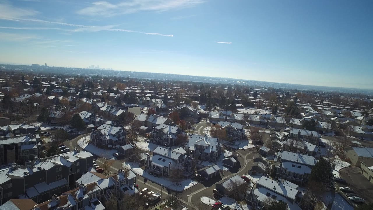 Early aerial frame in Hidden Lake, Colorado showing rows of houses, pale winter snow, leafless trees, a wide horizon, and no visible people.