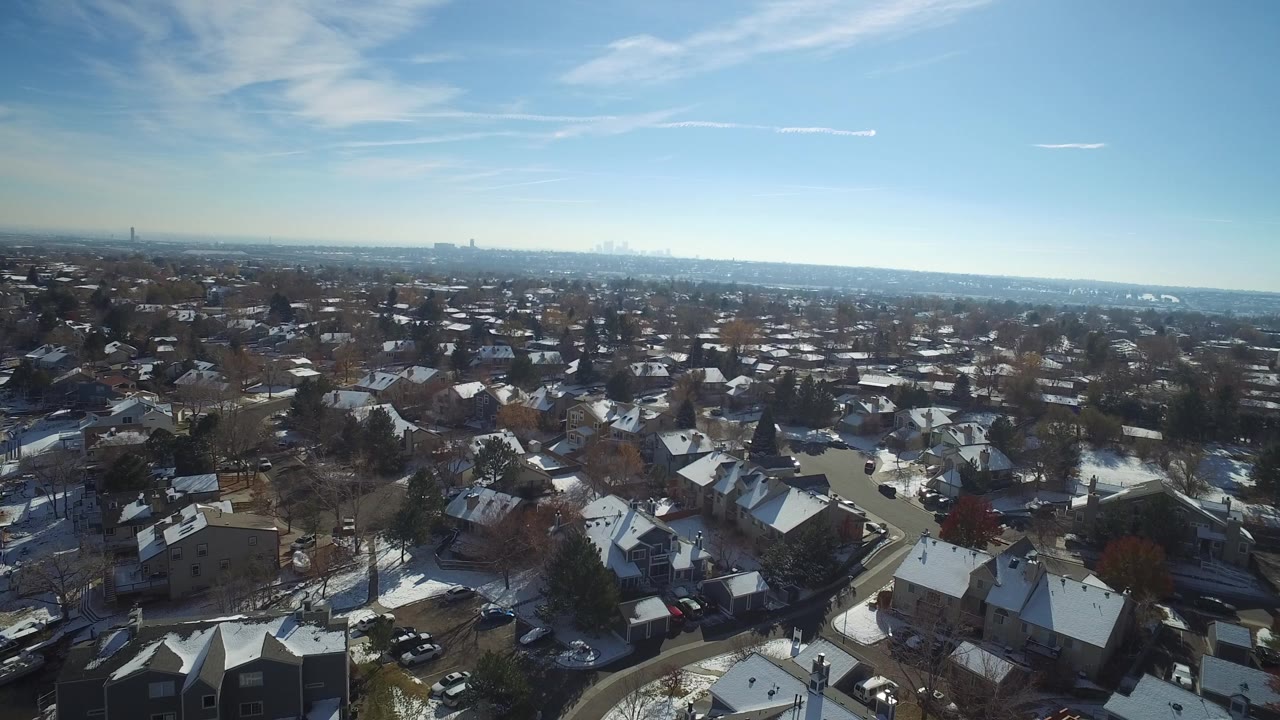 Aerial view over snowy residential roofs and streets under blue sky.