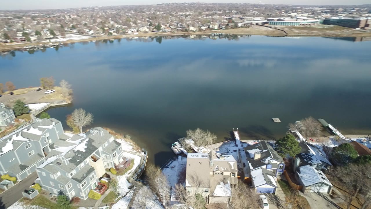 Aerial view of green lake beside snow-dusted townhomes