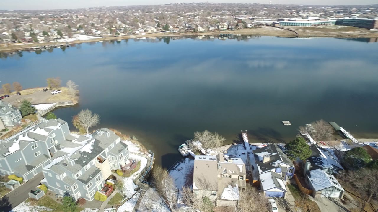 Aerial frame over Hidden Lake, Colorado showing open water, clustered rooftops at the near shore, small docks, winter trees, and no visible people.