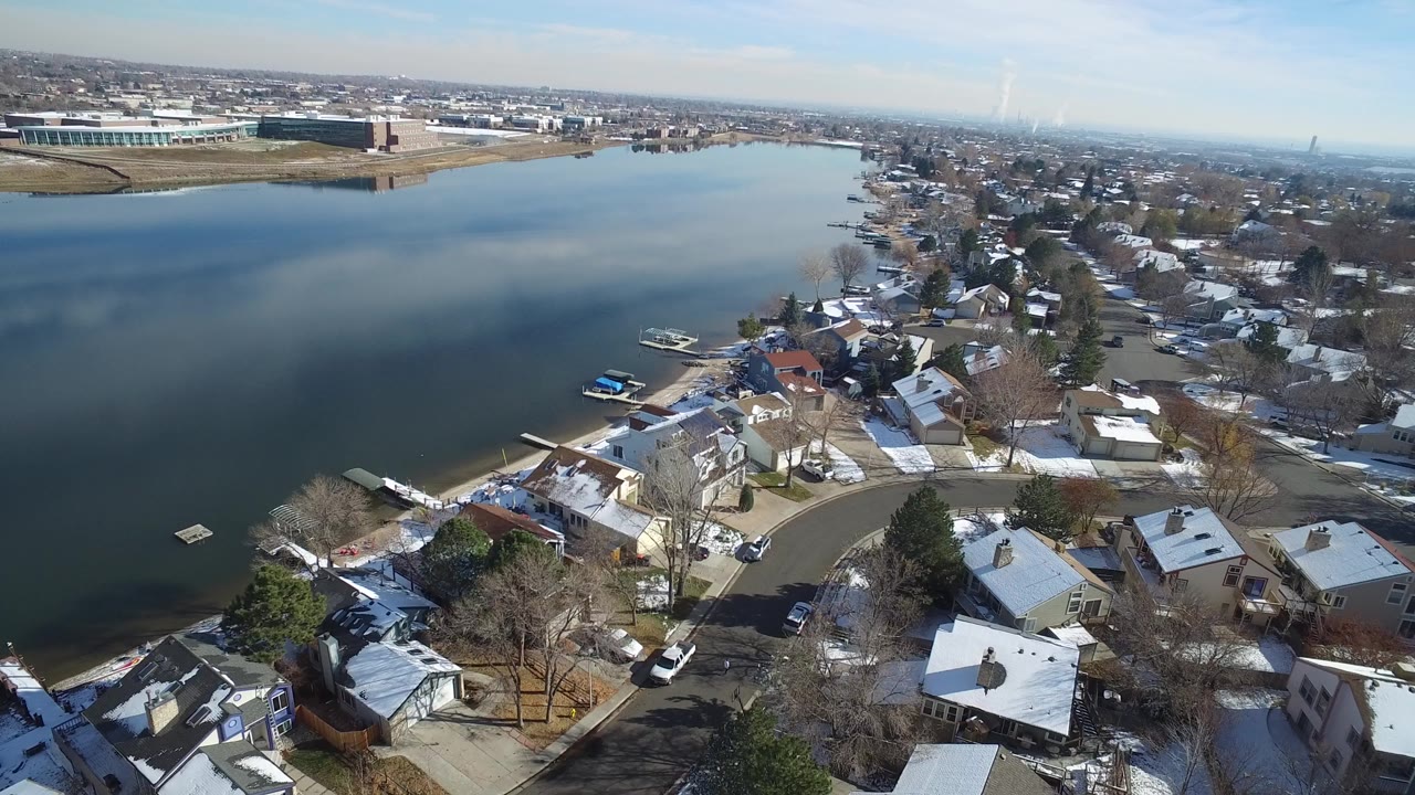 Aerial view of a lakeside neighborhood with snow on rooftops and docks along the shore.