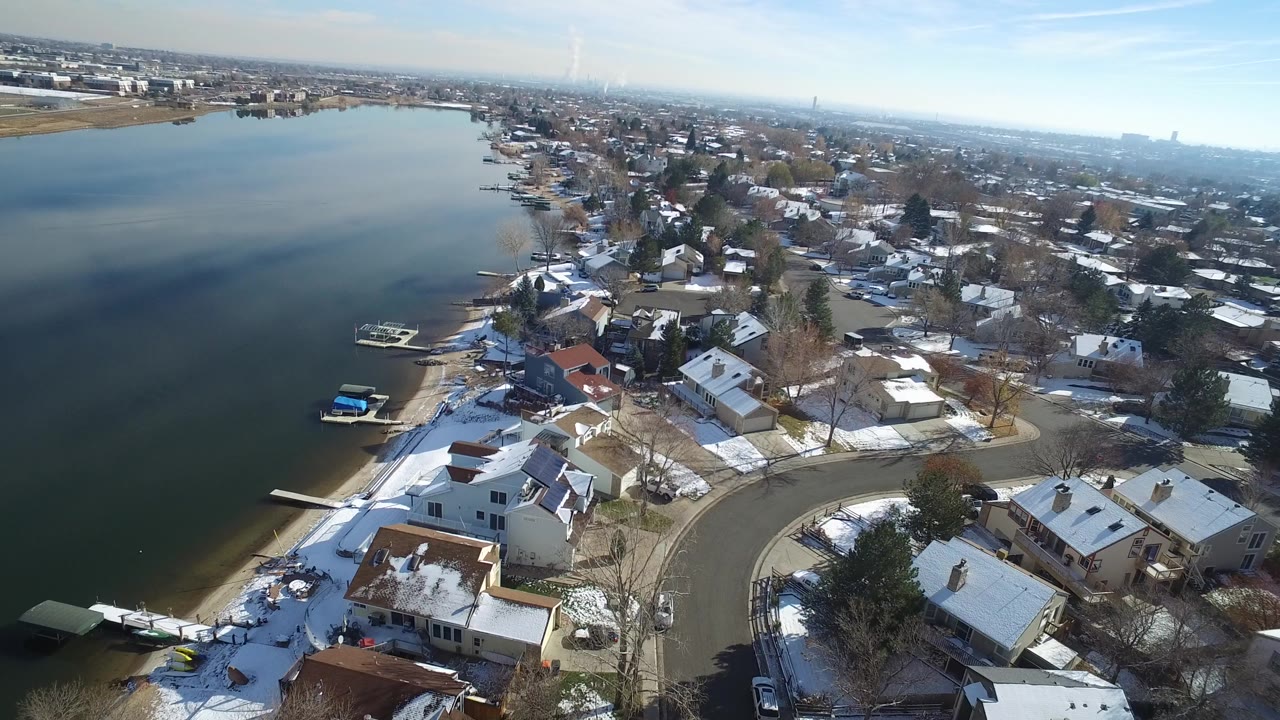 Aerial view of a lake shoreline with snow-covered homes and curved residential streets.