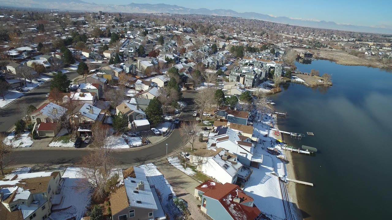 Aerial view of lakeside homes beside blue water with snow patches.