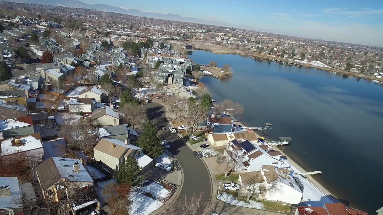 Aerial view of houses beside a lake with snow on rooftops and yards.