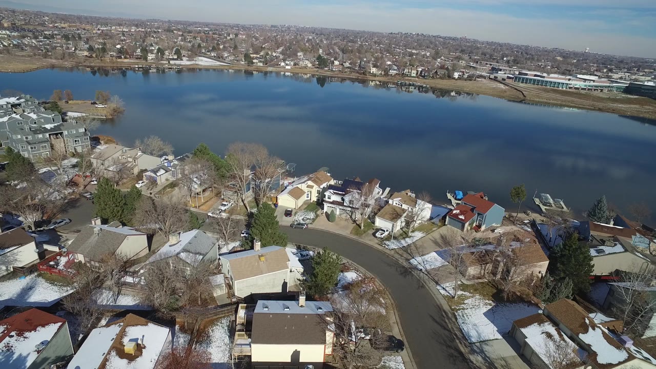 Aerial view in Hidden Lake, Colorado looking past residential rooftops and parked cars toward the wide lake and low horizon, with no visible people.