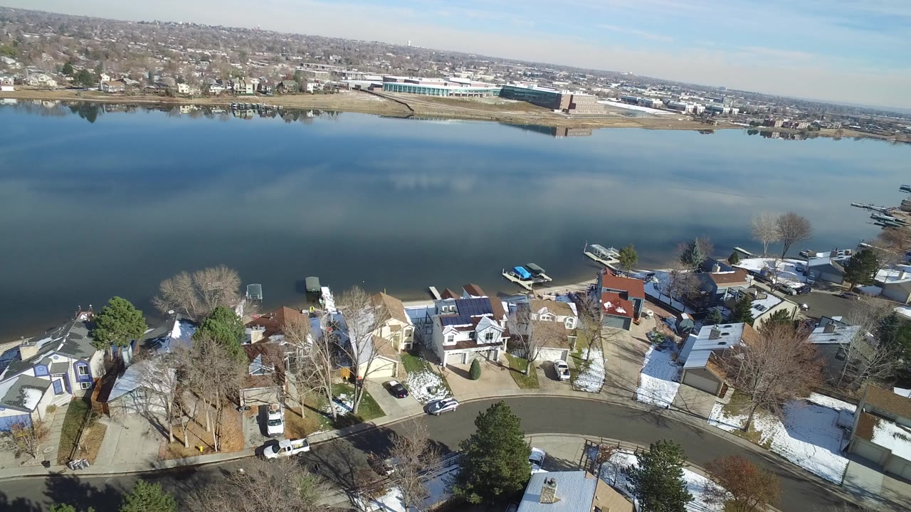 Aerial view over lakeside houses, a curved street, docks, and broad water.