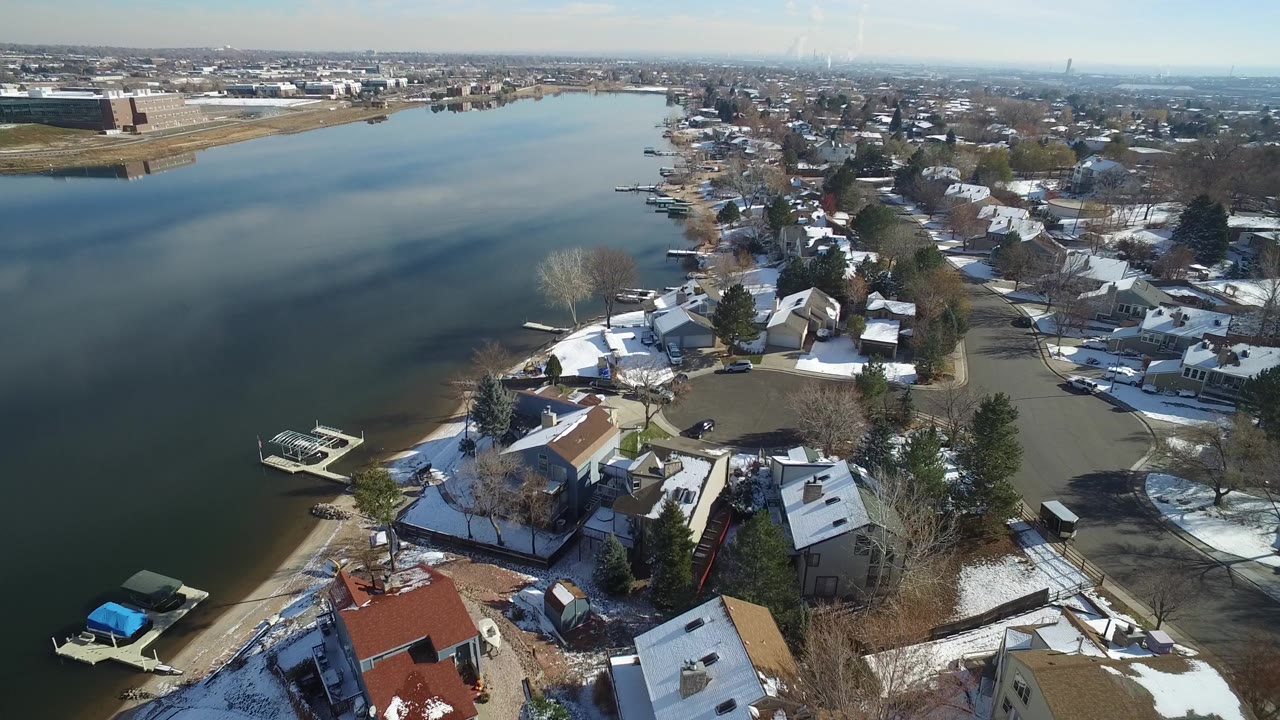Aerial view in Hidden Lake, Colorado, showing the lake widening left of frame while snow-covered houses, bare trees, docks, and a residential road fill the right side, with no visible people.