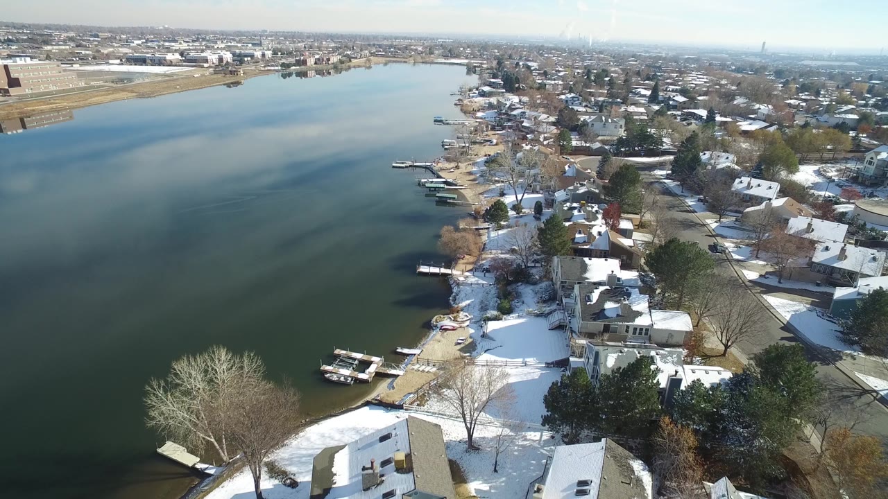 Aerial shoreline scene with calm water, homes, docks, and snow-covered yards.
