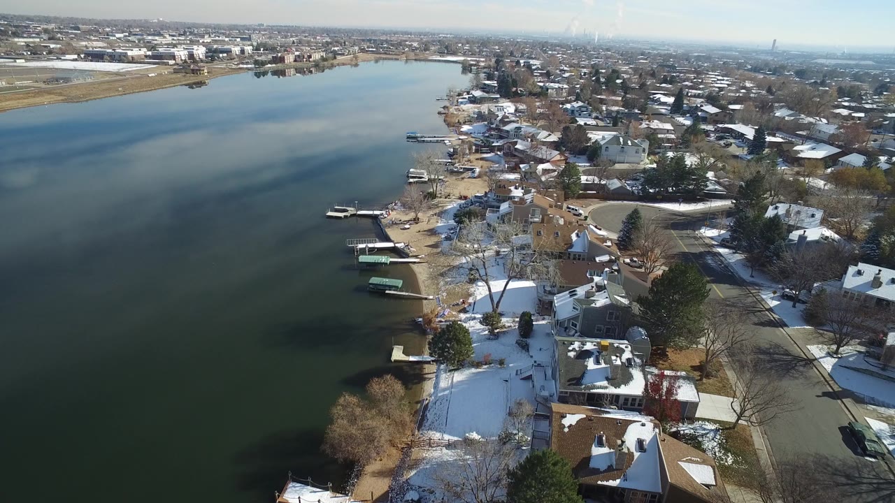 Aerial view over Hidden Lake, Colorado, with dark water on the left, snow-dusted houses and small docks along the shoreline, and no visible people.