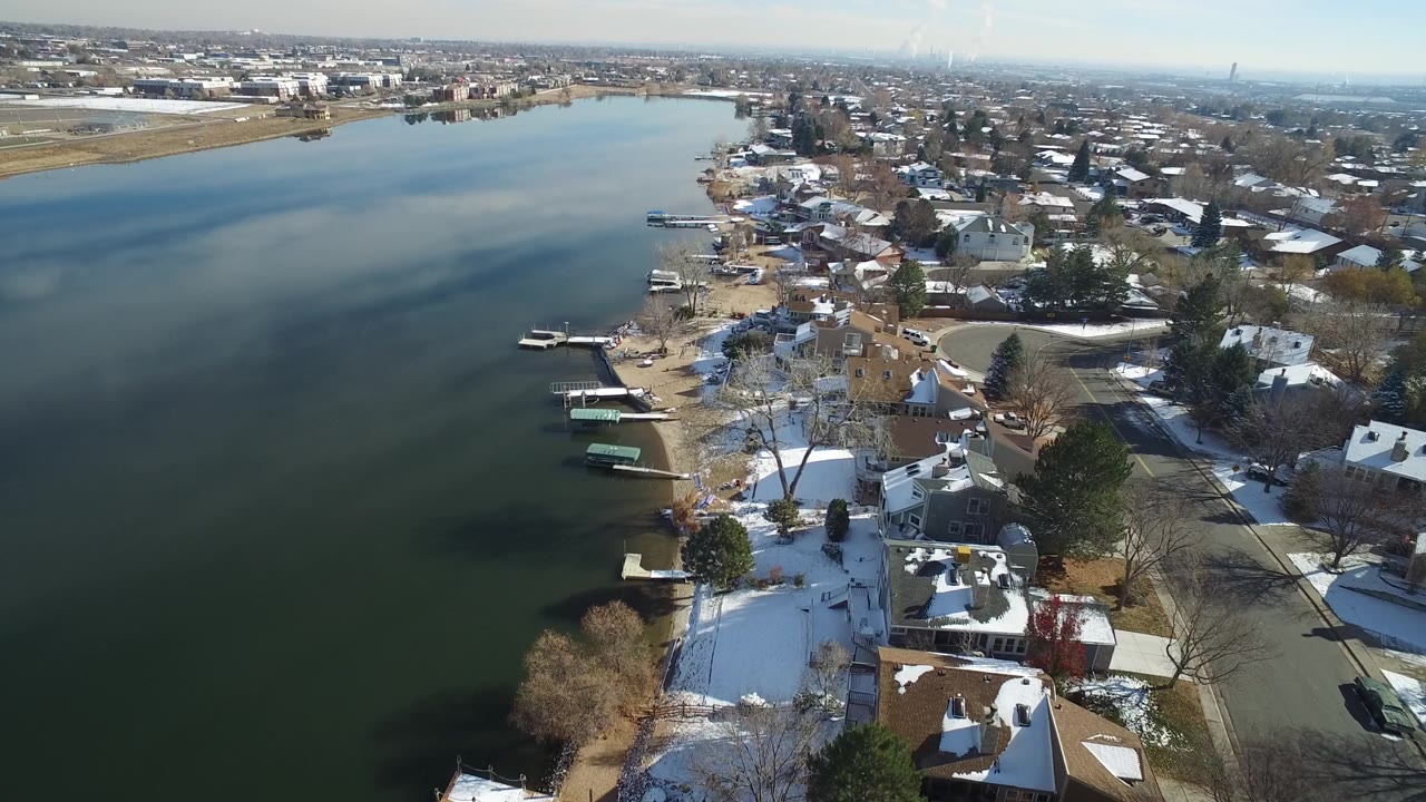 Hidden Lake, Colorado aerial frame showing more of the curved residential road, shoreline homes, docks, snow patches, and no visible people.