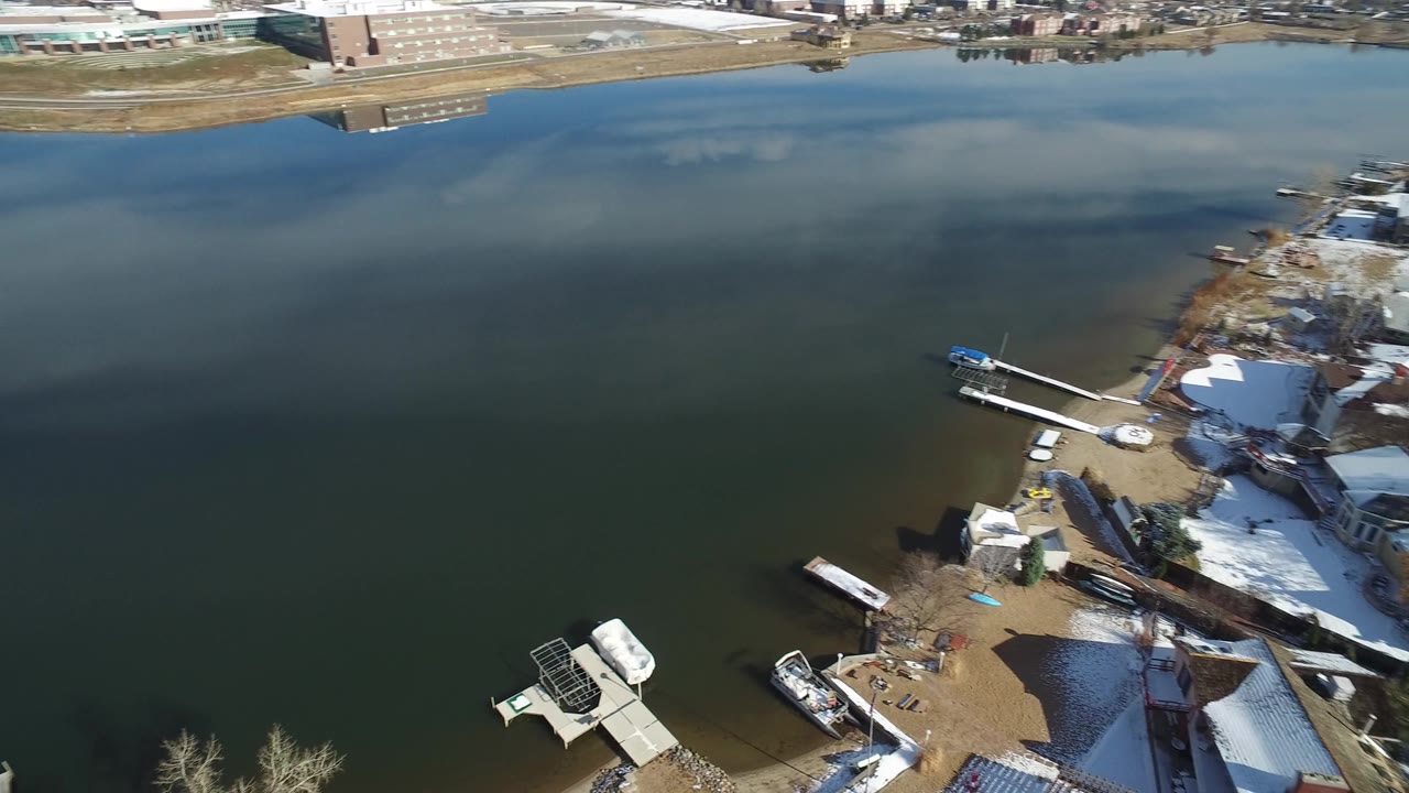 Aerial view in Hidden Lake, Colorado, showing broad lake water, a developed shoreline, snow-covered yards, docks, and residential buildings below the camera.