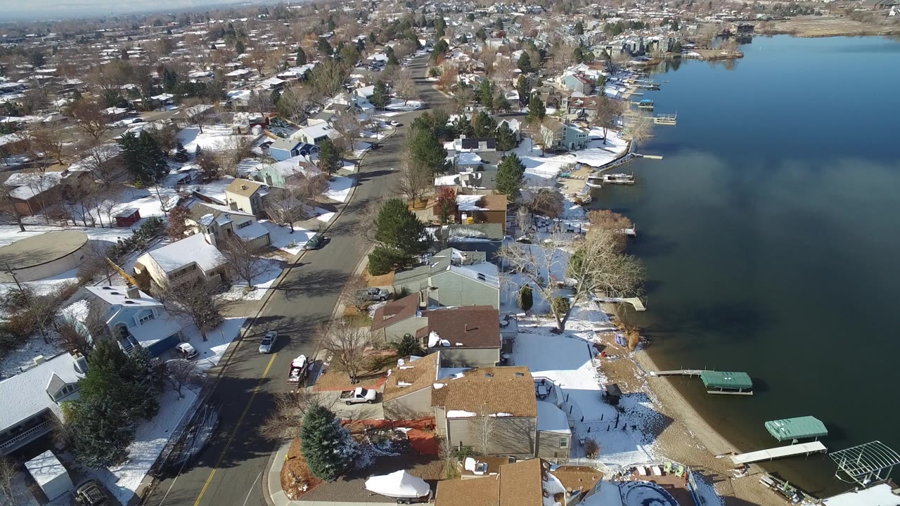 Aerial view of lakeside homes, roads, snow patches, and dark water.