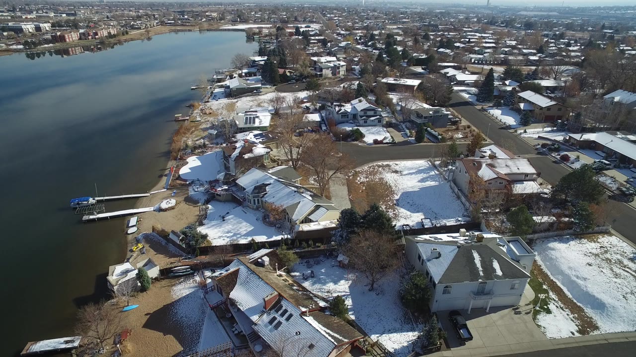 Aerial view of lakefront homes with snow-patched yards and docks.