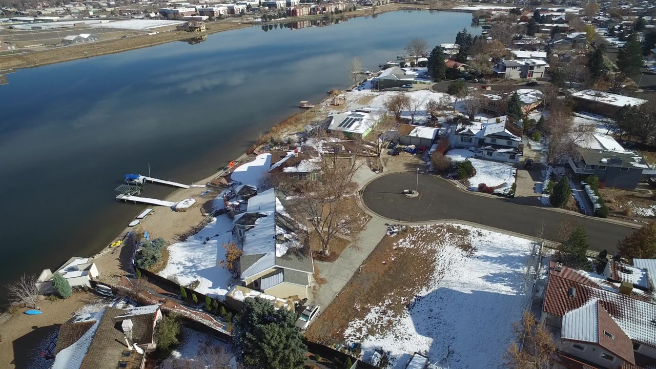 Aerial frame over Hidden Lake, Colorado showing houses, docks, bare trees, patchy snow on yards, blue lake water, and no visible people.