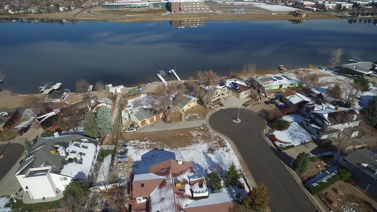 Aerial view in Hidden Lake, Colorado with the cul-de-sac centered, residential roofs below, shoreline docks above, and still dark water beyond, with no visible people.