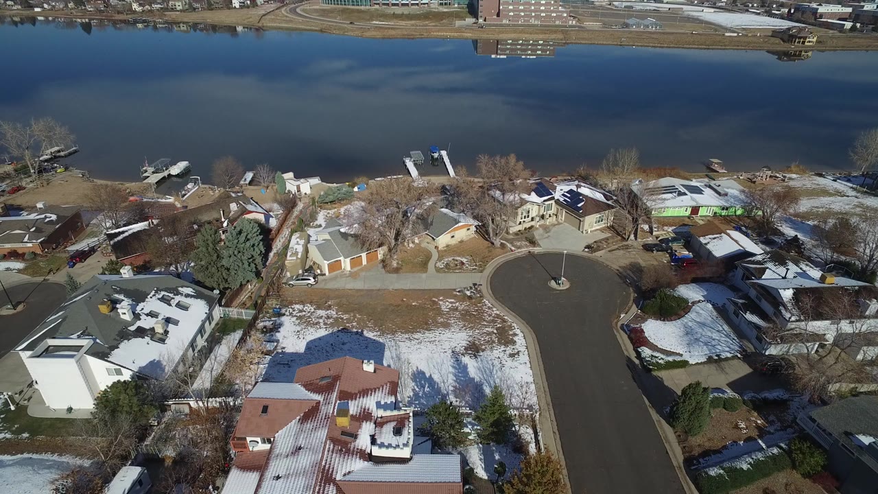 Aerial view of homes beside a blue lake with snow patches on lawns.