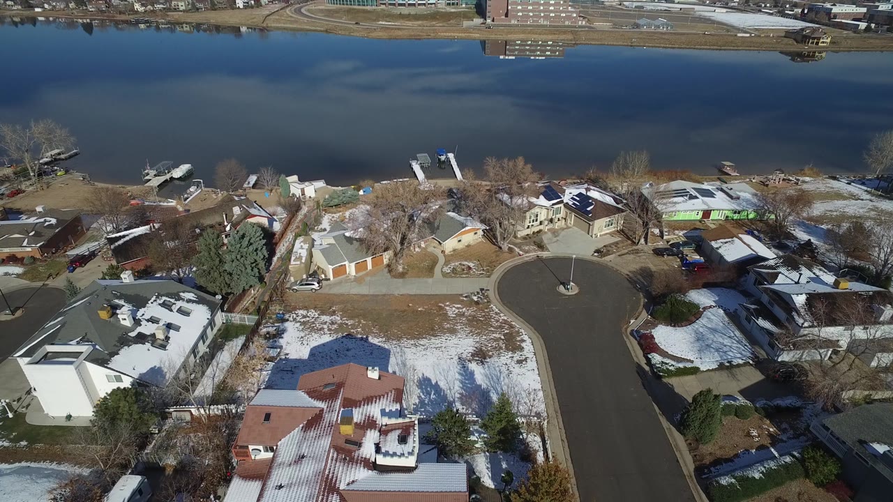 Hidden Lake, Colorado aerial view with the cul-de-sac centered, rooftops below, docks near the shoreline, patchy snow, and no visible people.