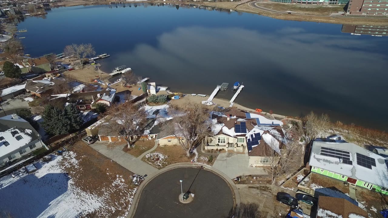 Aerial frame in Hidden Lake, Colorado, with a circular residential street in the foreground, snow on roofs and lawns, docks along the shore, and no visible people.