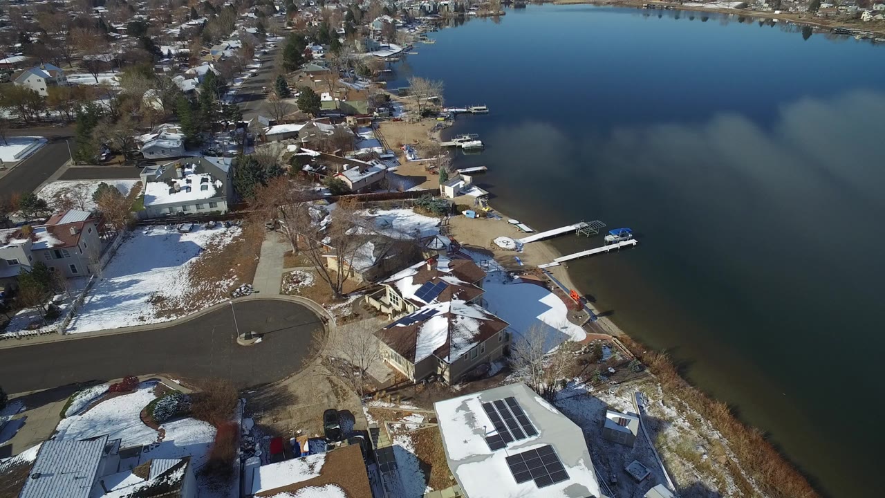 Aerial view of snow-dusted homes beside a lake with docks and a curved street.