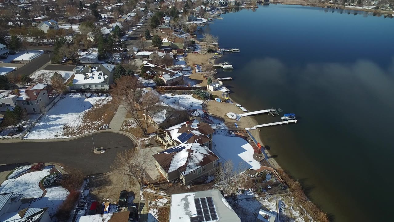 Aerial view of snowy homes beside dark lake water and small docks.