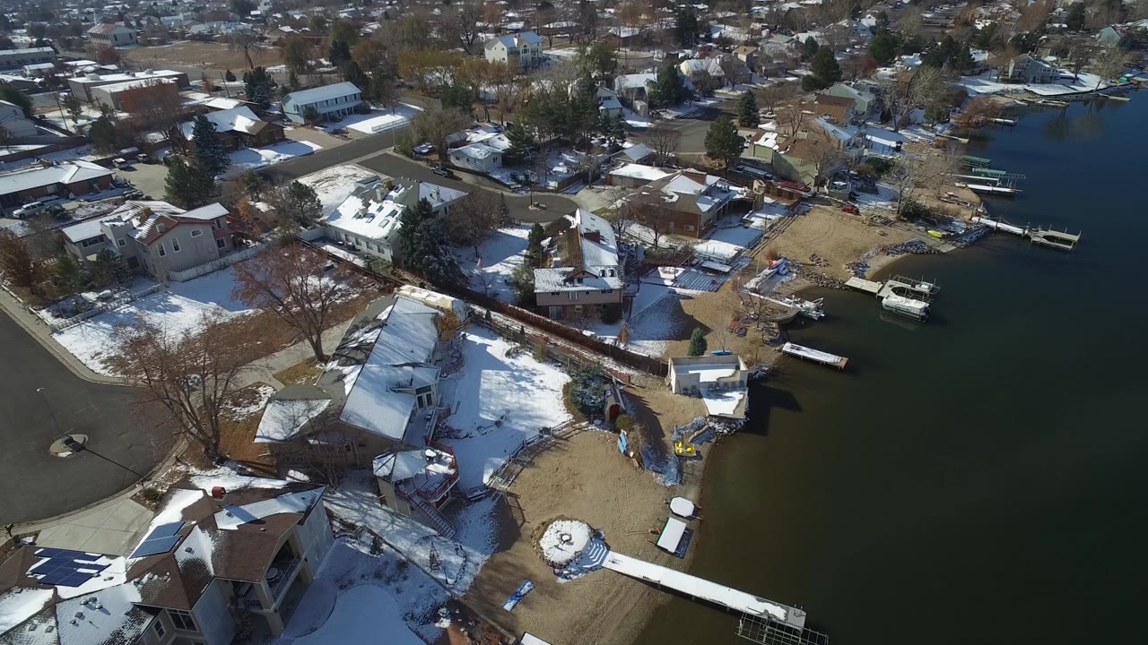 Snowy residential shoreline with houses, piers, and a small boat near the water.