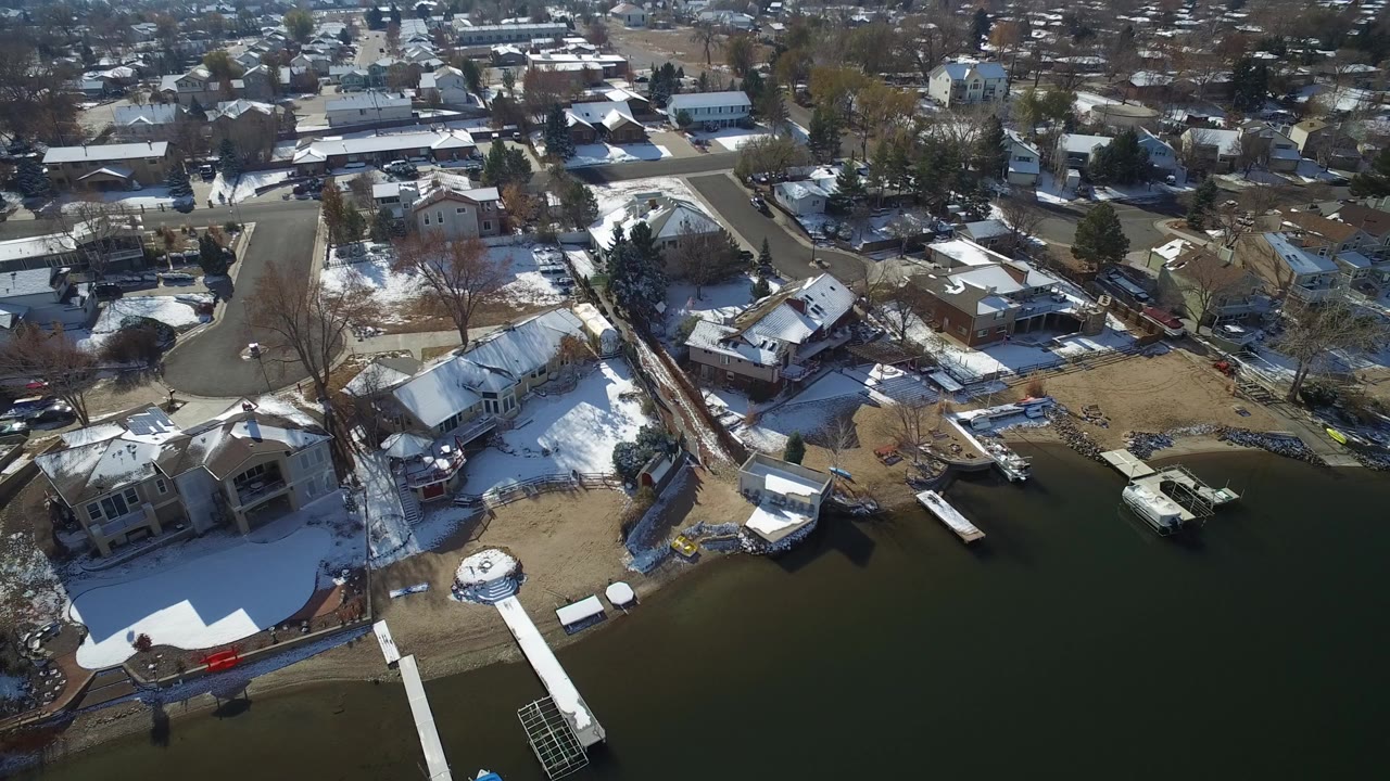 Aerial view of lakeside homes, docks, snow patches, and residential streets.