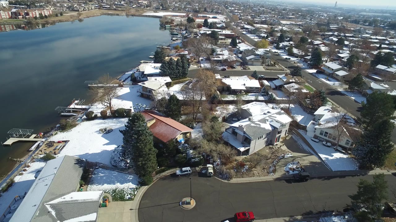 High aerial frame in Hidden Lake, Colorado with the pond along the left edge, a red-roofed building near the lower center, white roofs, bare trees, and no visible people.