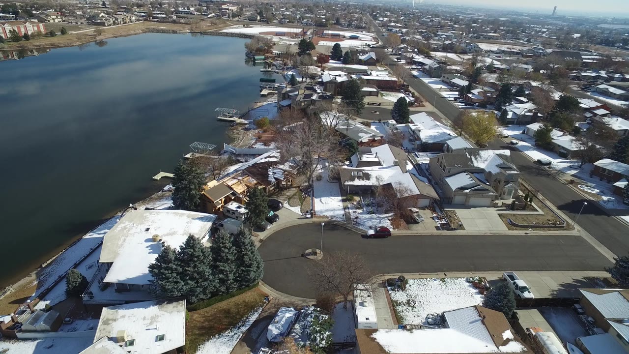 Aerial frame over Hidden Lake, Colorado, showing a broad section of lake, a curved cul-de-sac, snow on roofs and lawns, docks along the shore, and no visible people.