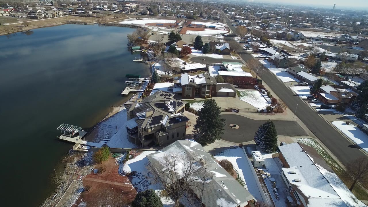 Aerial view of a lake beside snow-dusted homes and a lakeside road.