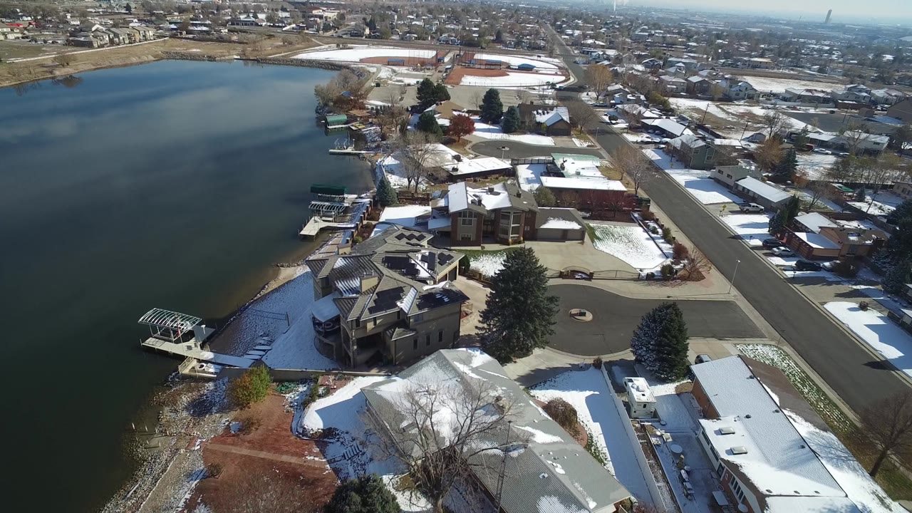 Aerial view in Hidden Lake, Colorado, showing the shoreline lower left, a cluster of private homes, boat docks, a straight lakeside road, patchy snow, and no visible people.