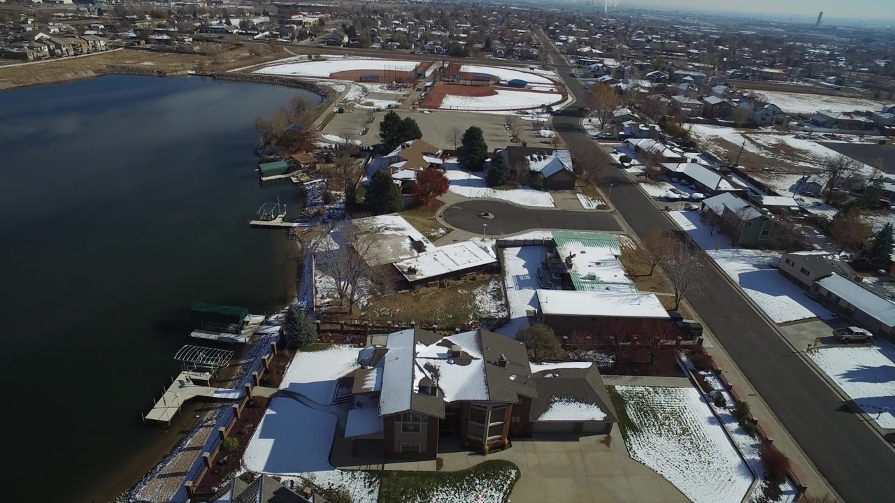 Aerial view over a lakefront residential street with snowy rooftops.