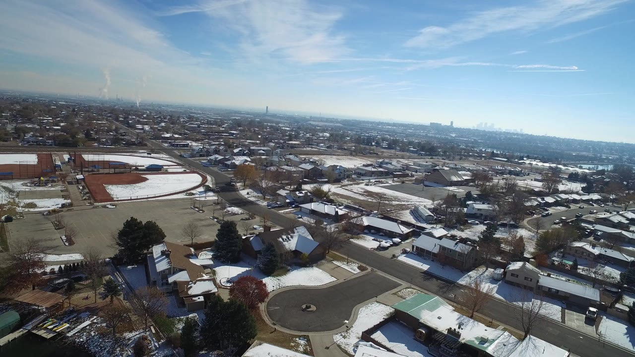 Snowy suburban streets and homes seen from above with a track at left.
