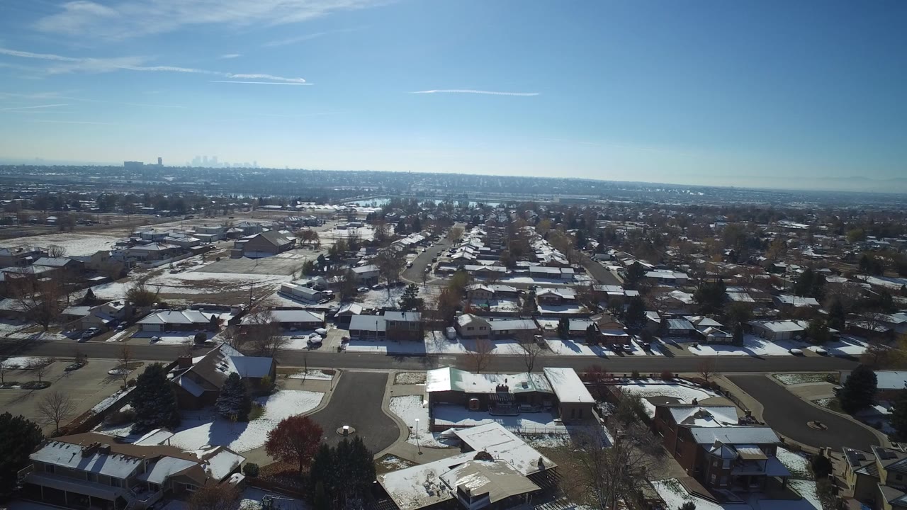 Aerial view over snow-dusted suburban homes and streets under a blue sky.
