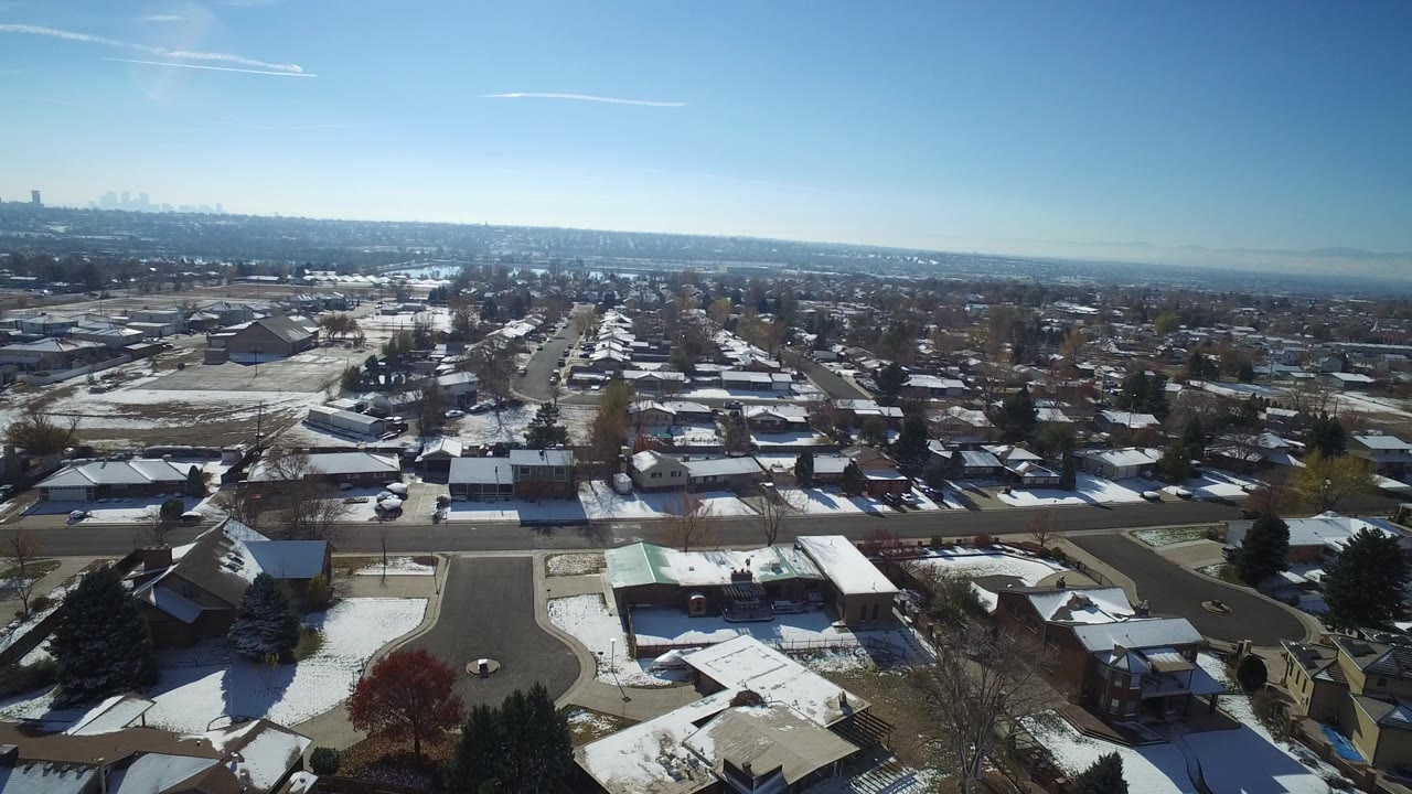 Aerial view over snowy suburban homes and streets under a blue sky.