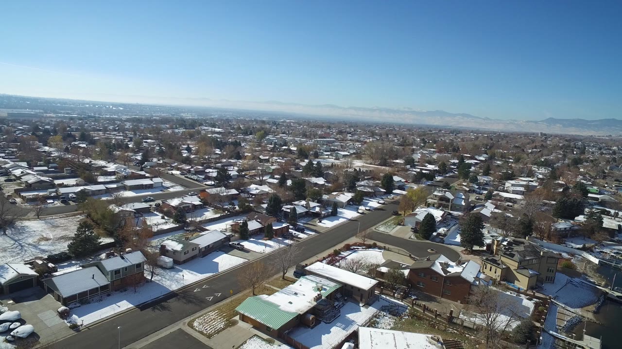 Snowy residential neighborhood seen from above with distant mountains.