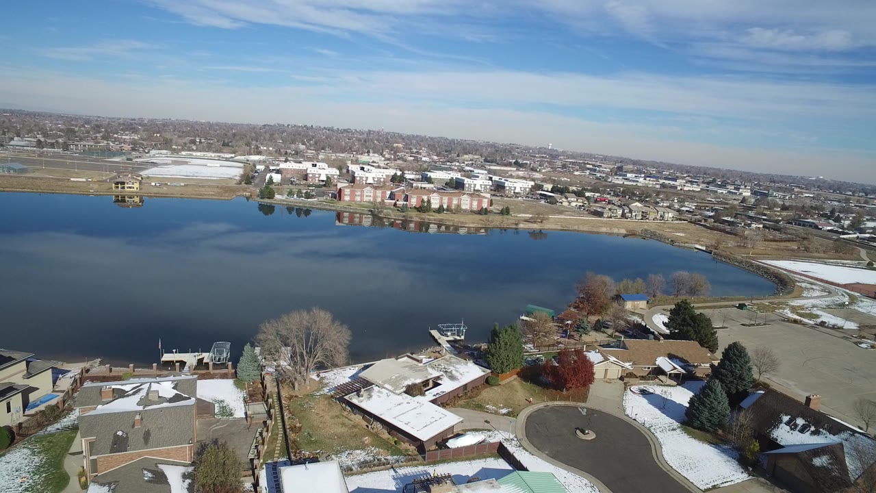 Aerial view of a lake beside houses and city streets with snow patches.