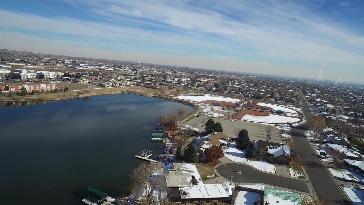Aerial view of a lake beside snowy residential streets and rooftops.