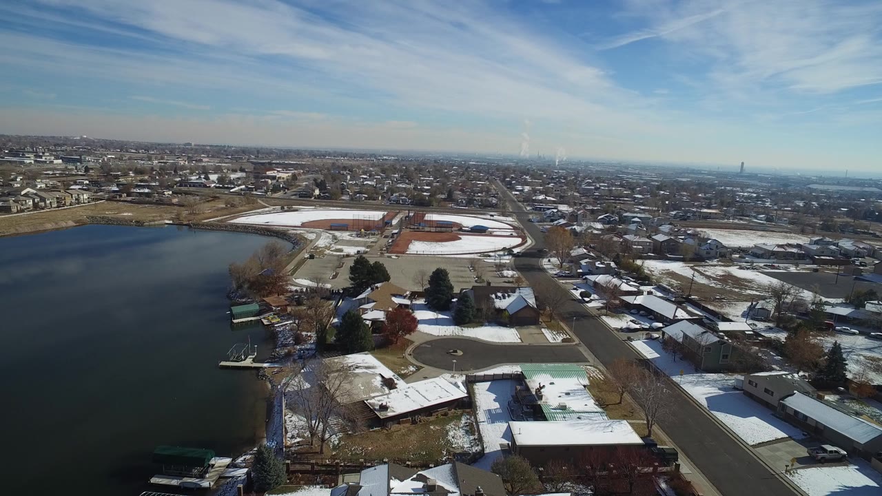 Aerial view of a lake beside snow-covered suburban homes and streets.