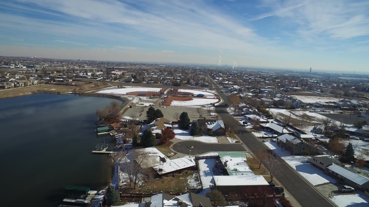 Aerial view across Hidden Lake, Colorado, showing the lake at left, shoreline homes and docks below, gridded streets beyond, pale winter ground, and no visible people.