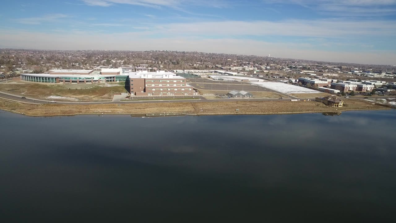 Aerial view over a blue lake toward low-rise buildings and distant neighborhoods.