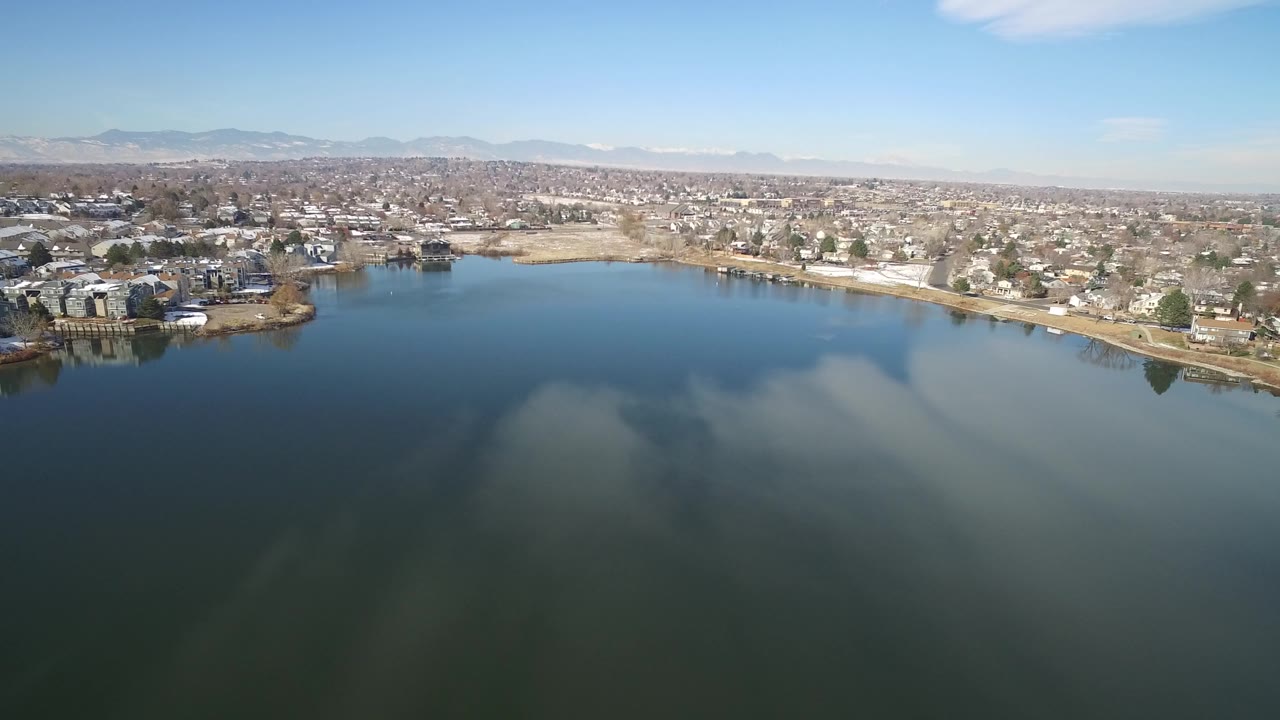 Aerial view over a blue lake toward shoreline homes and distant mountains.