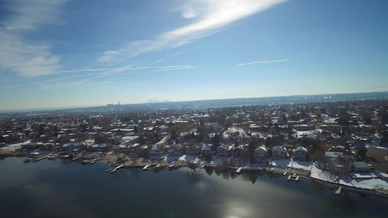 Drone-style view of lakeside houses, docks, and a broad blue sky.