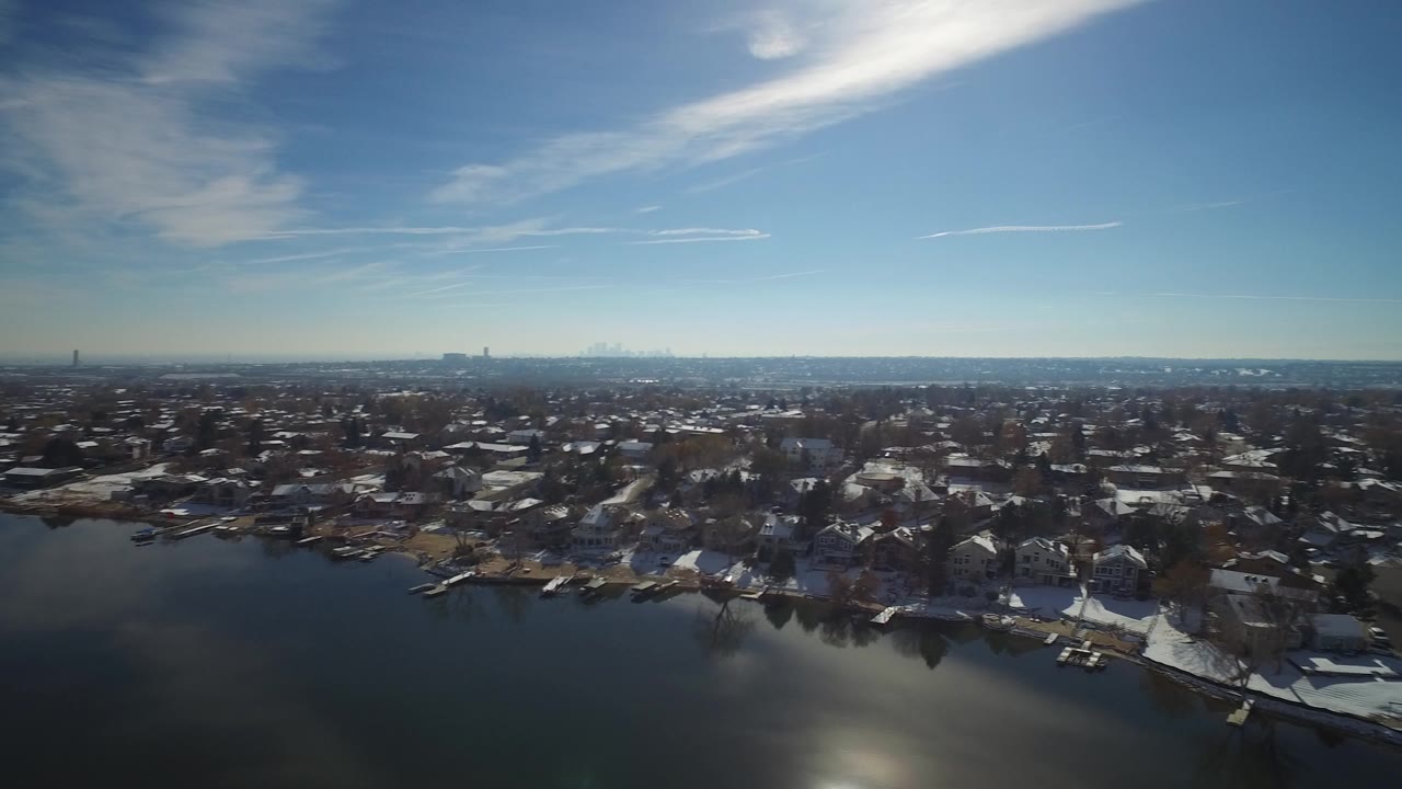Wide aerial view over a lake and snow-dusted residential shoreline.