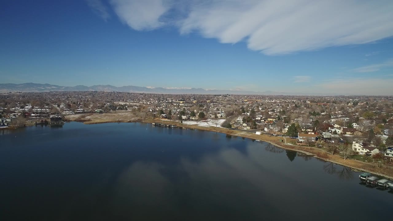 Aerial view over a lake toward a residential shoreline and distant mountains.