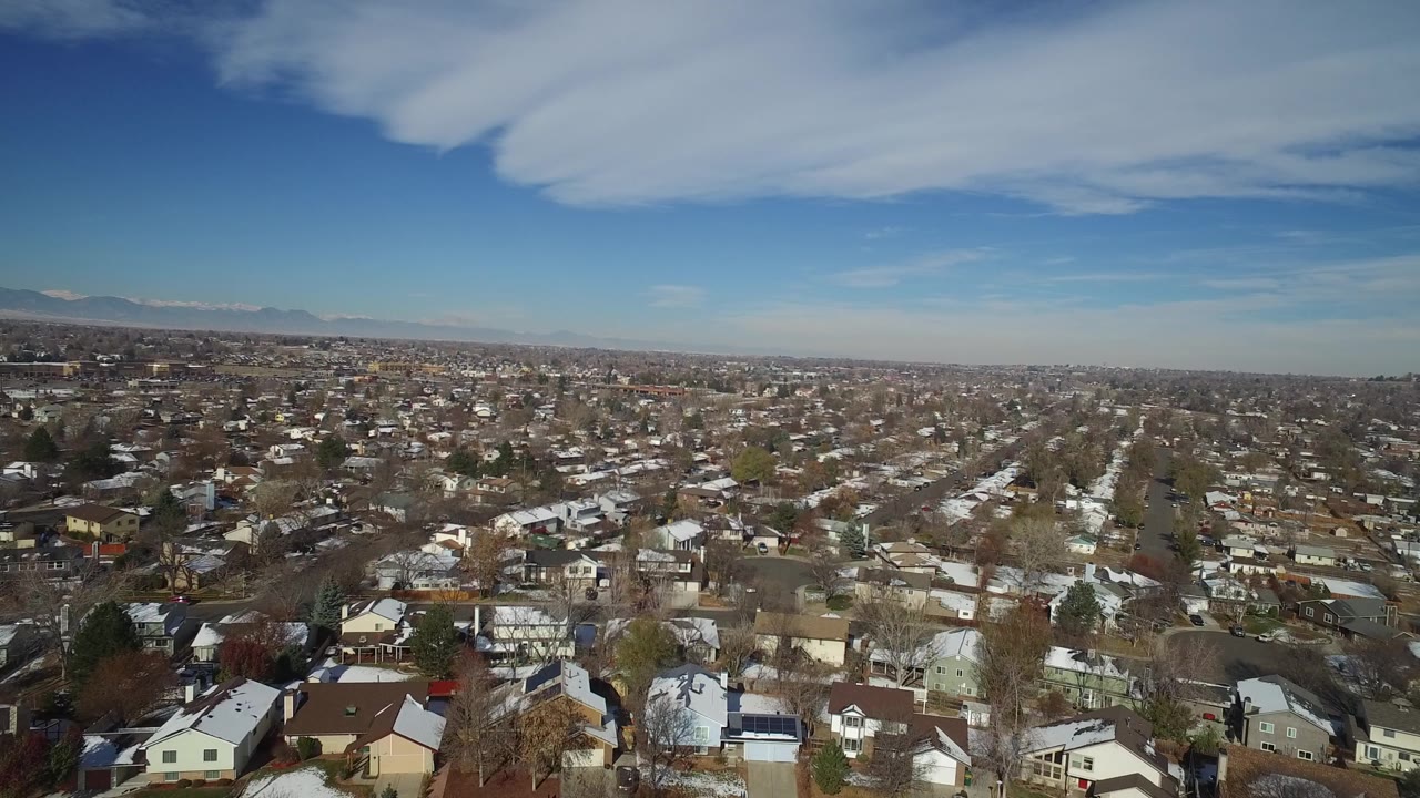 Aerial frame over Hidden Lake, Colorado rooftops and neighborhood blocks, with snow on some roofs, leafless trees, a long horizon, and no visible people.