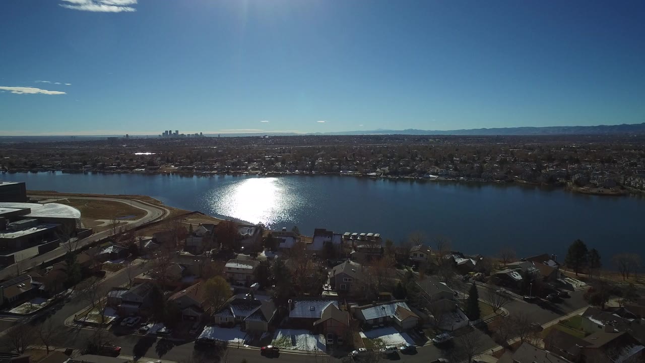 Aerial view over homes, a lake, distant skyline, and mountains.