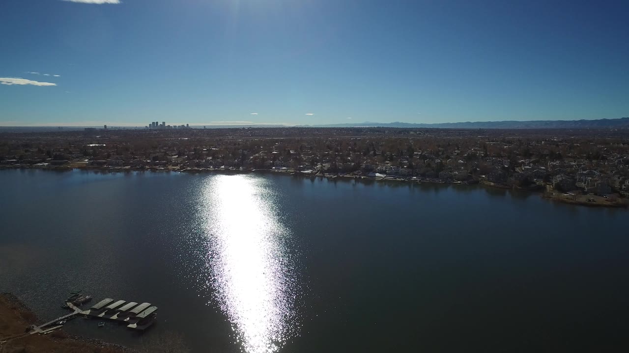 Aerial view over a lake with strong sun reflection and distant skyline.